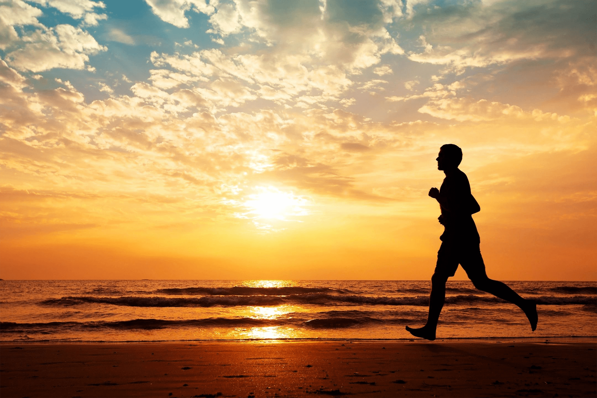A man running on the beach at sunset.